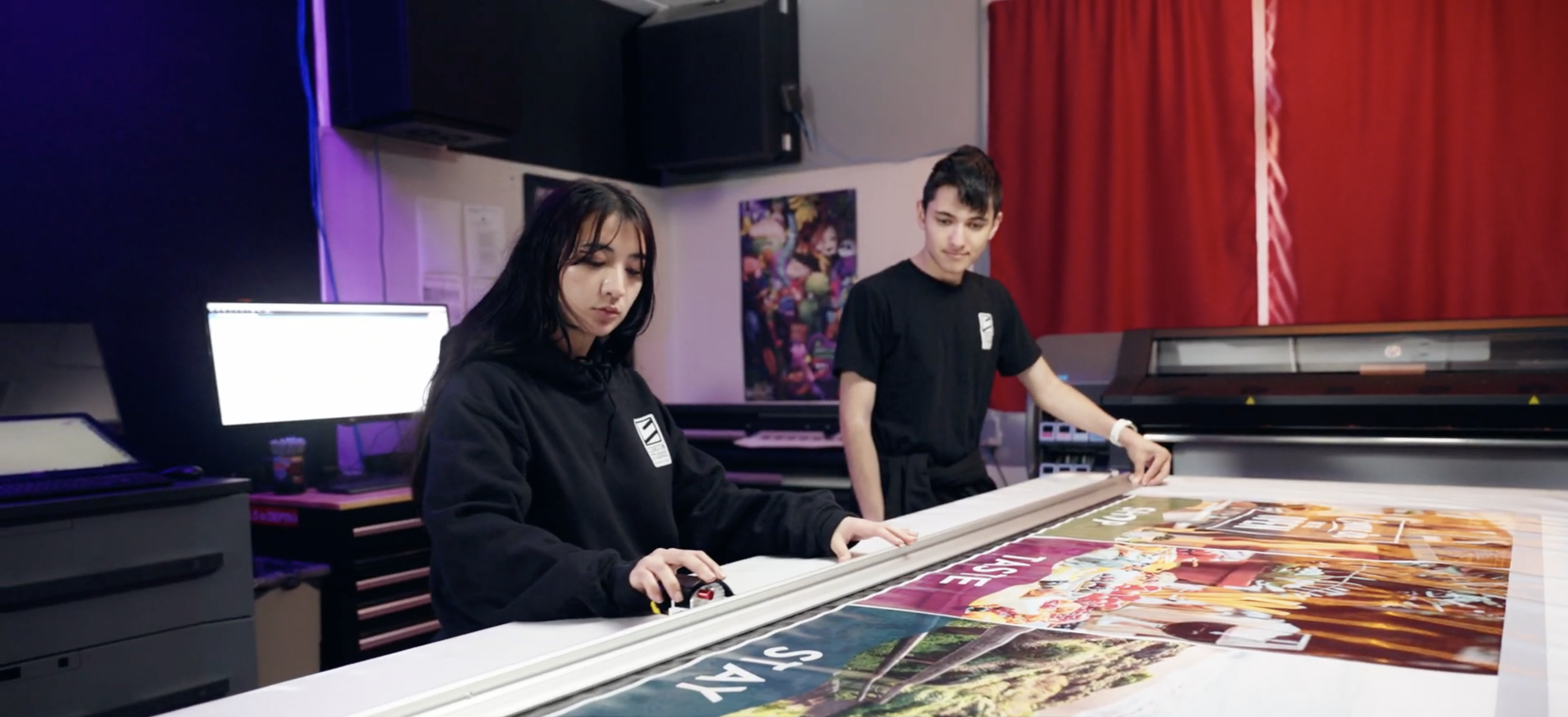 Coastin’ Studios student workers, Carolina Hernandez and Gabe Vargas, assist with a print job.